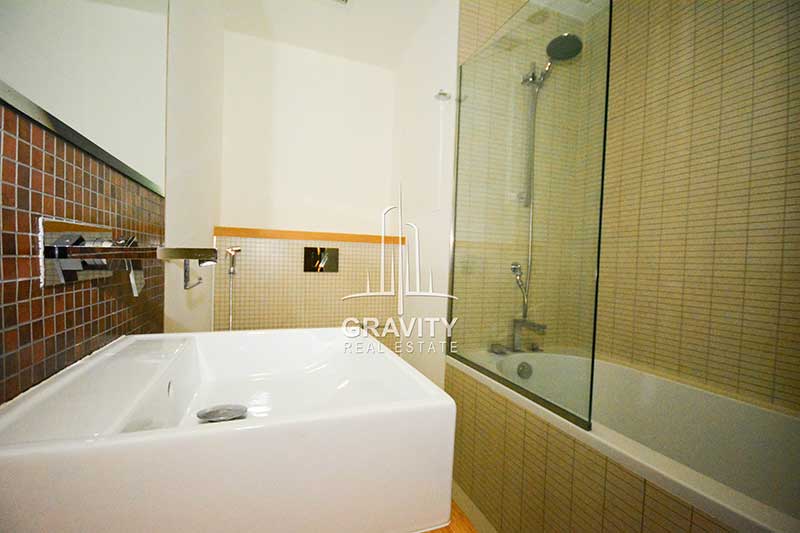 Bathroom-in-apartment-for-sale-in-Al-Raha-Beach-having-partioned-bathtub-a-shower-head-and-squared-shaped-wash-basin