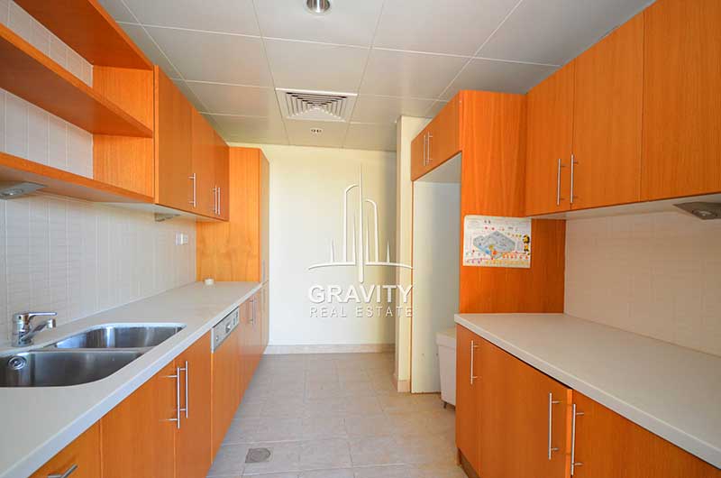 Elongated-Kitchen-with-brown-colored-wooden-cabinets-and-shelves-washbasin-in-a-townhouse-in-Al-Raha-Garden