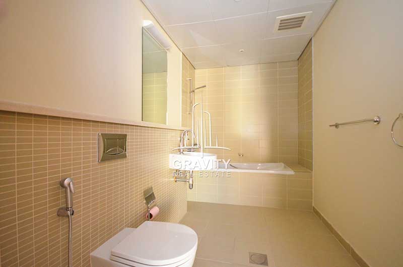 Elongated-toilet-with-brown-rectangular-tiles-on-the-walls-having-a-bathtub-a-mirror-a-wash-basin-in-Al-Raha-Garden