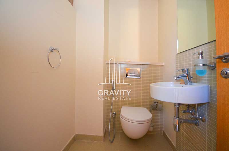 Fully-fitted-toilet-in-a-3-bedroom-townhouse-in-Al-Raha-garden-having-browned-colored-rectangular-tiles-on-the-walls