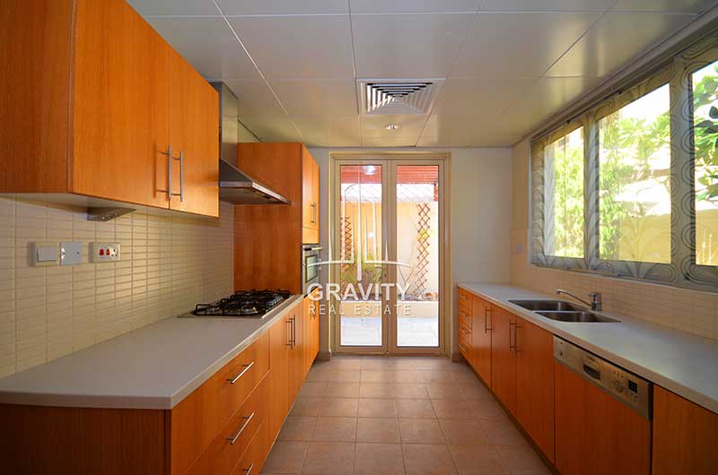 Horizontal-spacious-kitchen-in-a-4-bedroom-villa-in-Al-Raha-gardens-having-wooden-cabinets-and-shelves