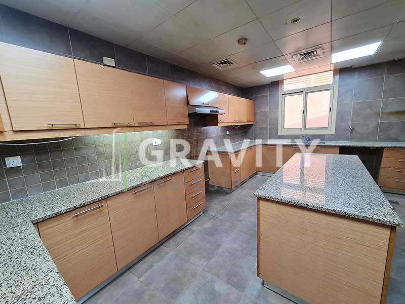 Kitchen-with-marbled-tabletops-and-wooden-cabinets-in-Al-Raha-Golf-Gardens-5-bedroom-villa-with-a-table-in-the-middle