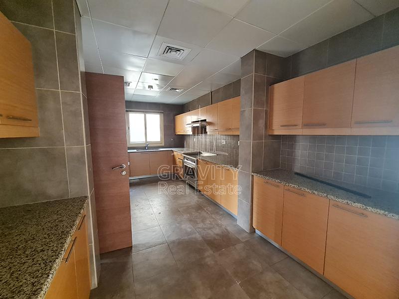 Long-kitchen-having-dark-grey-tiles-on-the-floor-and-the-walls-wooden-cabinets-exhaust-and-stove-in-Al-Raha-Golf-Gardens