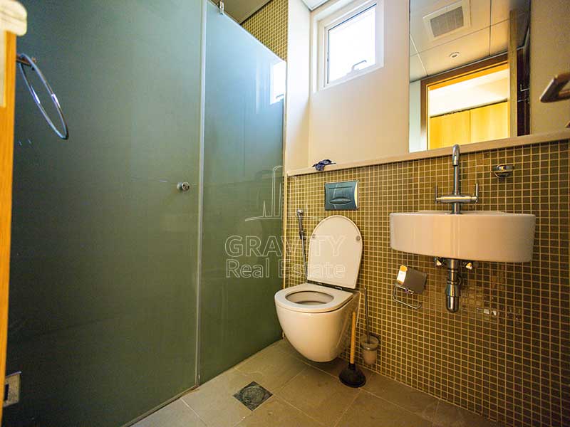 Toilet-in-Al-Raha-Garden-house-having-a-partition-for-shower-mini-square-tiles-large-mirror-and-sink