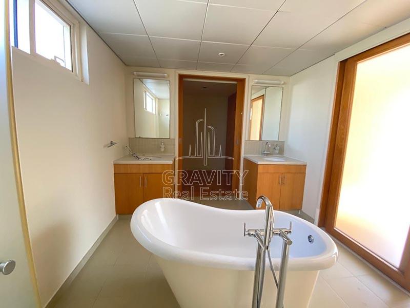 Toilet-in-a-villa-in-Al-Raha-Gardens-that-have-bathtub-in-the-center-and-with-a-doorway-in-the-middle-and-wash-basins-and-mirror