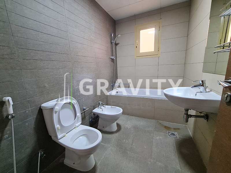 Toilet-with-grey-colored-tiles-on-the-walls-a-bathtub-and-sink-and-a-mirror