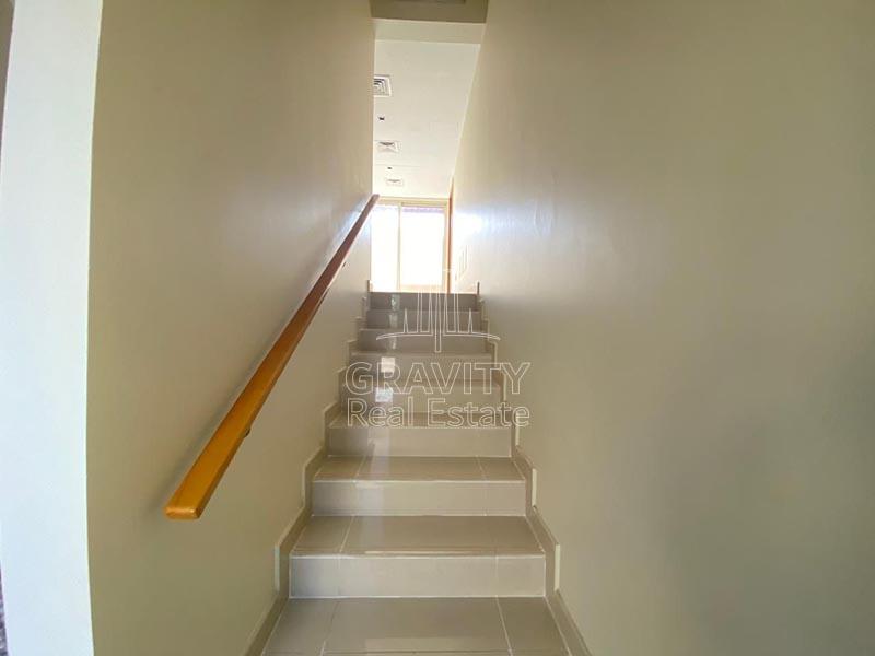 narrow-staircase-leading-to-the-floor-above-has-grey-colored-tiles-and-a-wooden-railing-on-the-side-wall-in-a-3-bedroom-villa-in-Al-Raha