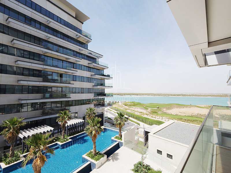 yas-island-mayan-balcony-with-pool-and-canal-view-with-palms-on-the-side-of-the-pool-and-buliding-facing-the-balcony-1