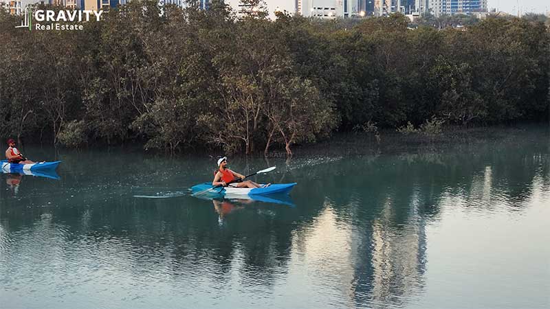 two-men-kayaking-in-turquoise-water-in-front-of-city-of-lights-promenade-surrounded-by-mangrove-trees