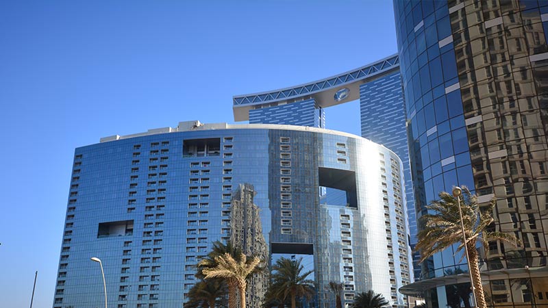 arc-tower-seen-from-the-bottom-up-with-greenery-and-palm-trees-near-its-entrance-and-the-gate-tower-behind-it