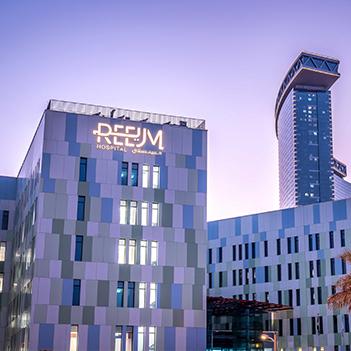 reem-hospital-exterior-during-the-evening-with-its-front-sign-brightly-lit-up-and-the-gate-towers-behind-it