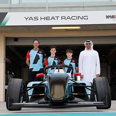 four-people-posing-behind-a-formula-one-vehicle-in-yas-racing-school