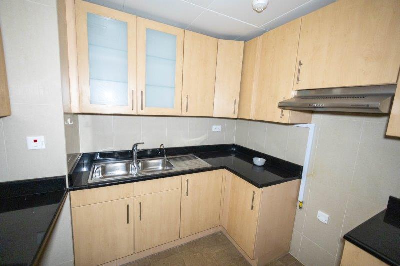 closed-kitchen-with-light-brown-cabinets-in-1-bedroom-apartment-in-sky-tower-al-reem