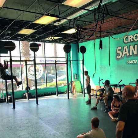 A man and woman inside a gym watching a guy perform chin ups