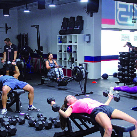 A woman holding 2 dumbells lying on a bench inside a gym